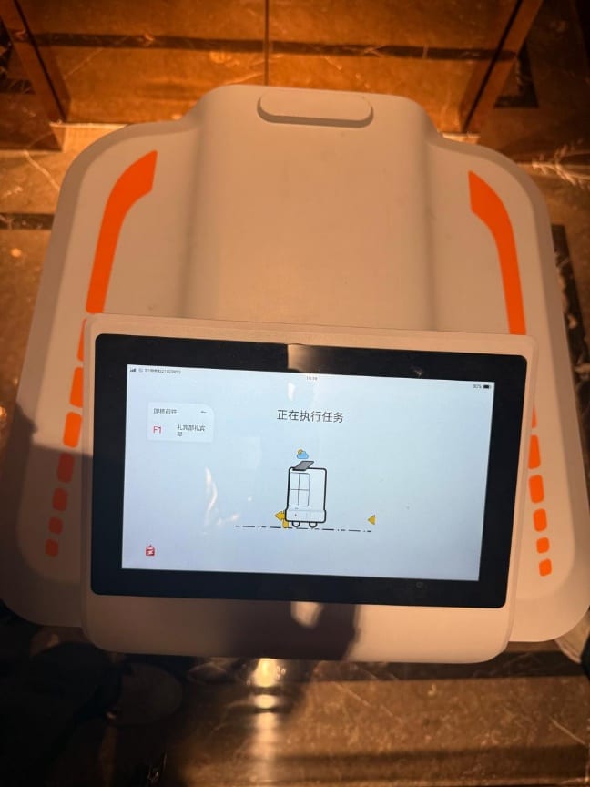 A concierge delivery robot with a touchscreen running a task, in a hotel lobby.