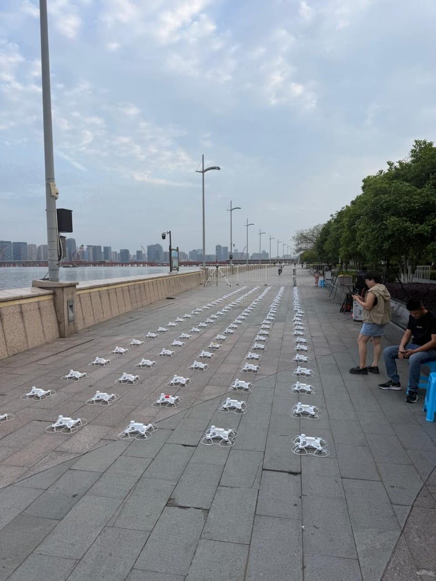 Rows of show drones lined up on a riverfront promenade waiting to fly.